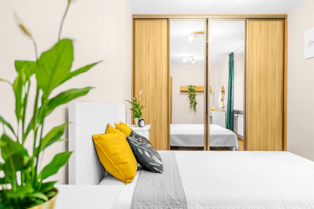 Bright bedroom with a white bed, yellow cushions and a mirrored wooden wardrobe (illustrative stock image)