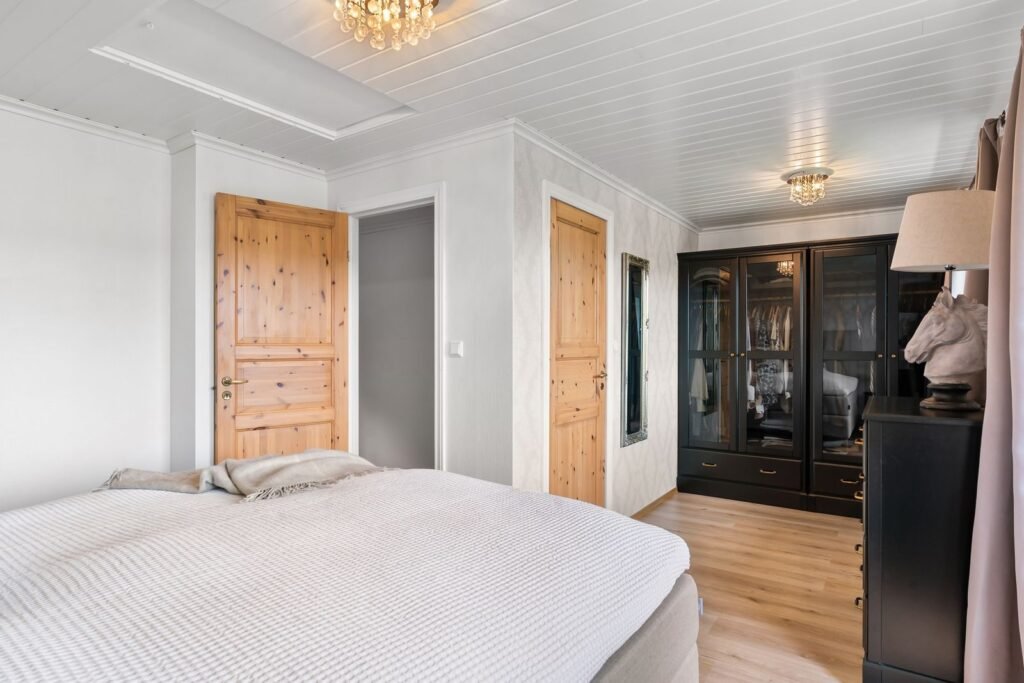 Bright bedroom with a white bed, wooden doors and a dark display cabinet (illustrative stock image)