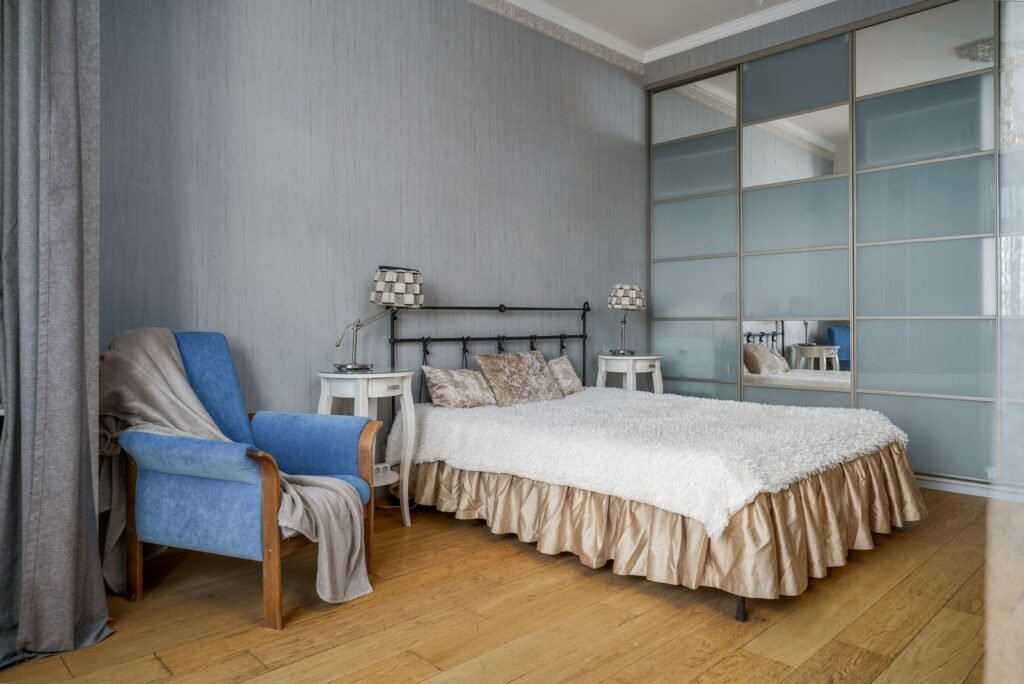 Bedroom with a metal-frame bed, armchair and a mirrored wardrobe (illustrative stock image)