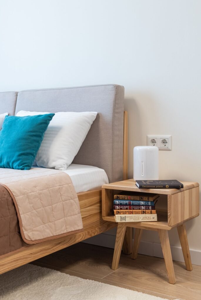 Bed with a grey headboard and a wooden open-shelf bedside unit (illustrative stock image)