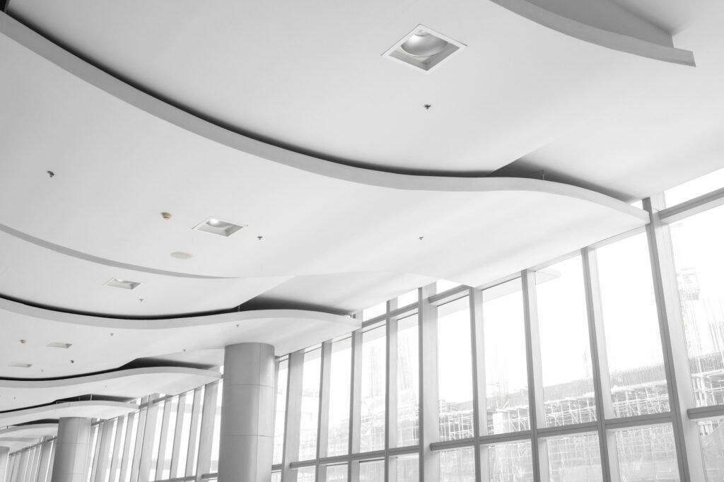 Curved white ceiling bands with recessed lights beside tall windows (illustrative stock image)