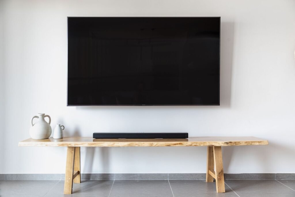 Large wall-mounted TV above a wooden bench in a white room (illustrative stock image)